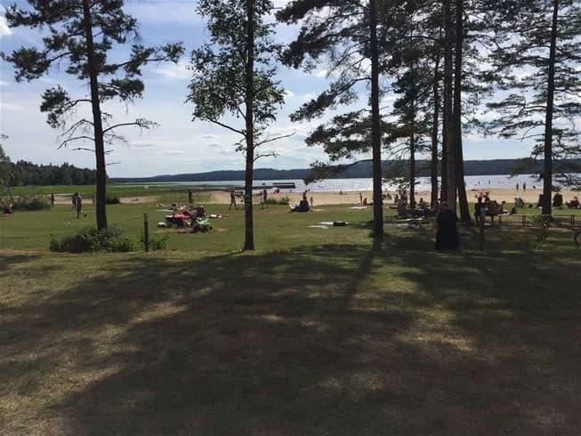 En öppen äng på Flatens camping med avkopplande utemöbler, omgiven av en grönskande natur som inbjuder till rekreation och semester.