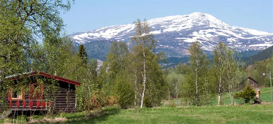 En naturskön campingplats i Åre, omgiven av bergslandskap och gröna träd. Enstaka hus syns bland kullar och växtlighet.