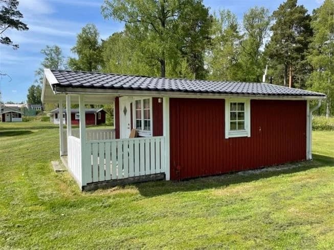 En charmig stuga av trä omgiven av grönska på Gökaskratts camping, med ett skuggigt tak och en rymlig bakgård.