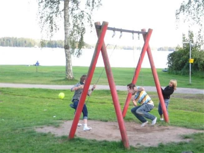 En lekplats vid Gökaskratts camping med gungor och balansutrustning, omgiven av grönska. Barn leker och njuter av utomhusaktiviteter i en parkmiljö.