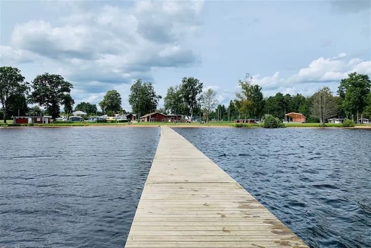 En sjö med klart vatten vid Gökaskratts camping, omgiven av grönskande träd och en mindre brygga som sträcker sig ut i vattnet.