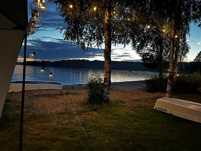 En solnedgång kastar långa skuggor över sjön vid Sandaholm restaurang & camping, med mjukt bakljus som skapar en lugn och fridfull atmosfär.
