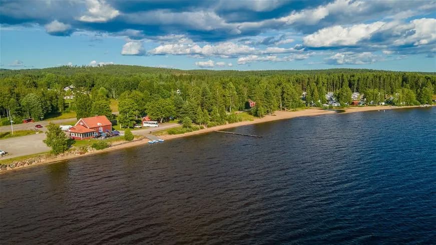 En vacker utsikt över en strand vid sjön med sand och små strandstugor i bakgrunden på Sandaholm restaurang & camping.