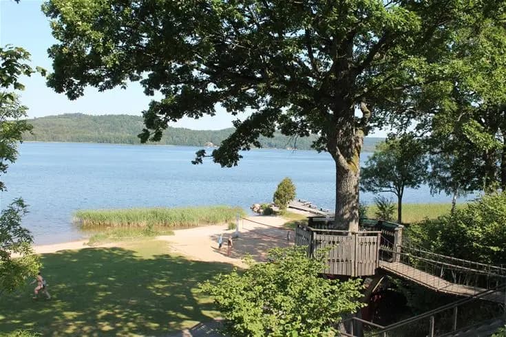 En rofylld sjö vid Skotteksgården Camping & Stugby med spegelblankt vatten och en omgivande kustlinje, idealisk för avkoppling och rekreation.