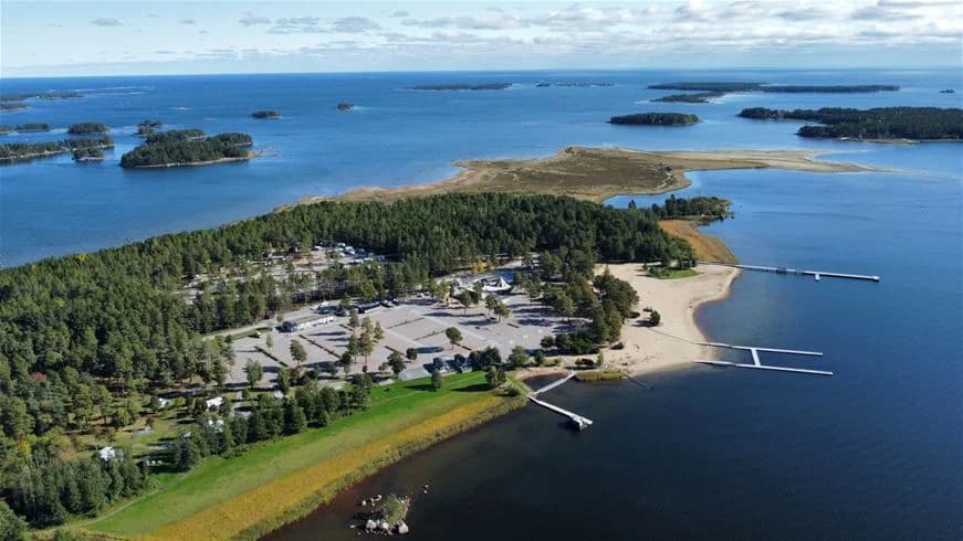 Flygfoto över Stenö havsbad & camping, med vy över vatten och kustlinje. Ön och strandremsan syns tydligt mot bakgrund av sjö eller hav.