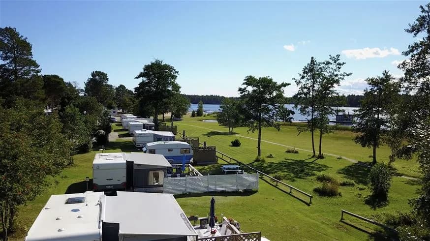 Flygfotografi över Stenö Havsbad & Camping med grönskande landskap, campingområden och en vik i bakgrunden.