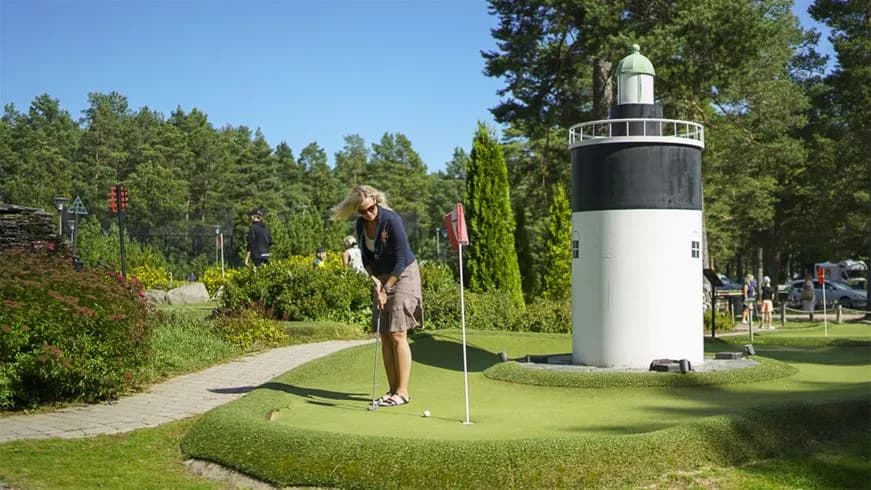 En grönskande campingplats vid Stenö Havsbad, med stora gräsytor, buskar och träd. Området är välskött och inbjuder till rekreation och aktiviteter, beläget vid en golfbana och erbjuder en trivsam utomhusmiljö för besökare.