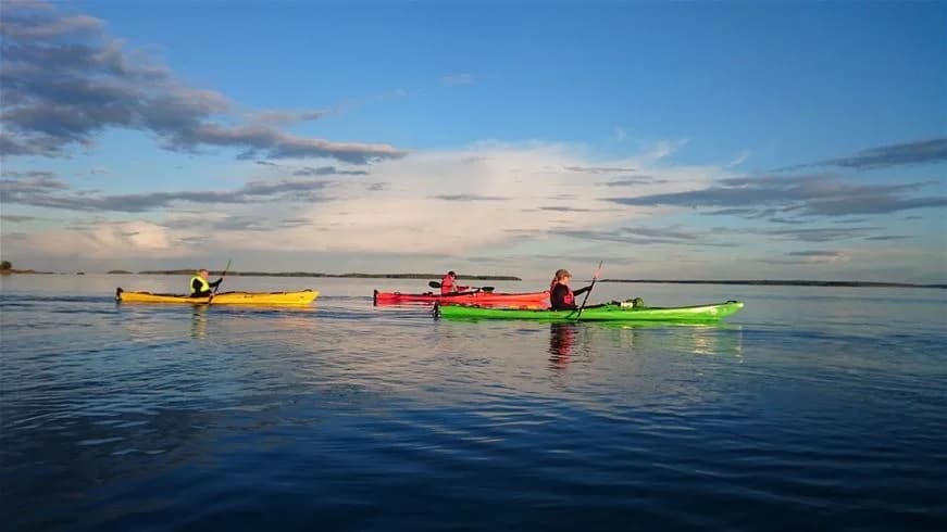 En person paddlar en kajak på det klara vattnet vid Stenö havsbad & camping, omgiven av vacker natur och friluftslivsmöjligheter.