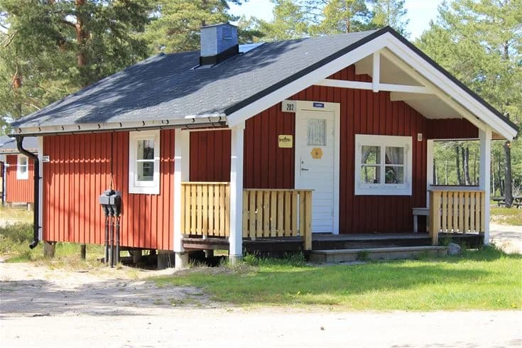 En trästuga med ett rött tegeltak omgiven av grönska på Stenö Havsbad & Camping.