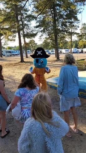 En grupp barn har roligt på Stenö havsbad & camping. De bär somriga kläder och kepsar, vilket ger en känsla av semester och fritid vid strandens rekreationsområde.