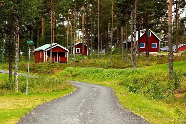 Bild av Åsarna Skicenter med en stuga omgiven av gräs, träd och skog i en lantlig miljö.