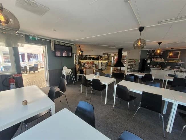 En mysig interiörvy av Älvkarleby Fiskecamping med träbord och stolar arrangerade på ett parkettgolv. Stora glasfönster låter naturligt ljus flöda in i den stilfullt inredda restaurangen.