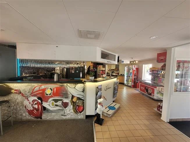 Bild av en snabbmatsrestaurang vid Älvkarleby Fiskecamping med en tydlig logotyp och reklam för matalternativ. Restaurangen är omgiven av naturliga omgivningar som förstärker campingens karaktär.