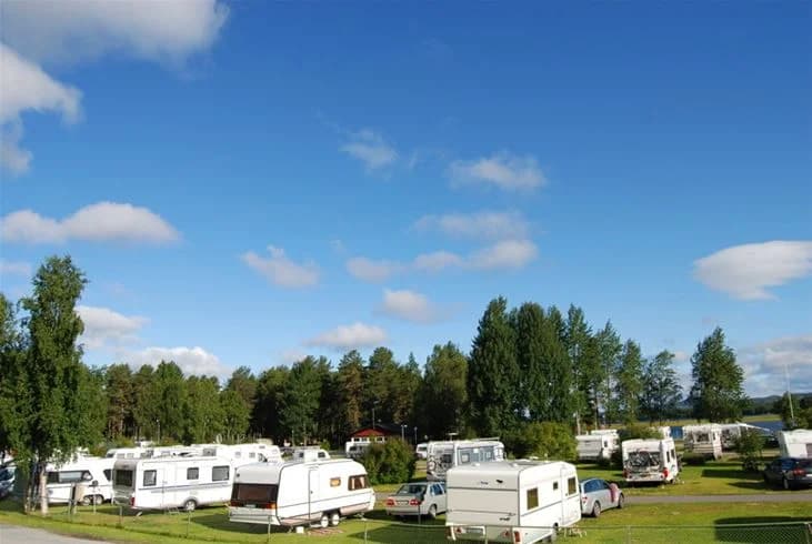 En husbil står parkerad på en grön gräsmatta vid Storuman Camping, omgiven av öppna ytor och klarblå himmel med några moln.