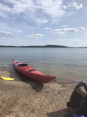 En kajak ligger vid strandkanten nära Malexander Camping, omgiven av en sjö och skogsklädda stränder.