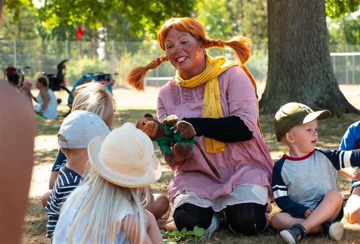 En grupp glada barn och vuxna har roligt tillsammans i en avslappnad miljö på Haga Park Camping & Stugor. Barnen bär kepsar och skrattar medan de leker i vårvädret.