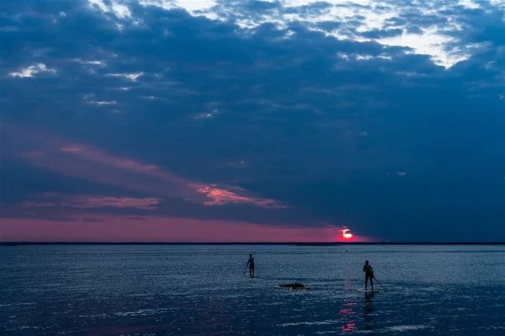 En vacker kvällshimmel med mjuka, blå färgnyanser och moln vid horisonten, solnedgångens varma glöd speglas i havet.