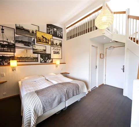 Ett rum på Lisebergsbyn med en bekväm säng täckt med vita sängkläder, omgiven av en stilren och mysig inredning som ger en hemtrevlig känsla.