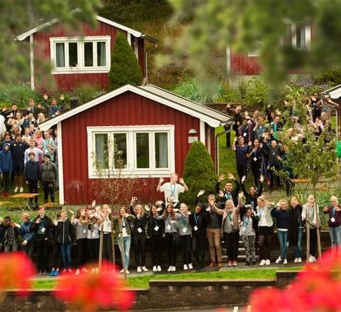 En stor grupp människor njuter av en utomhusceremoni på Lisebergsbyn, omgivna av grönska och glada leenden. Det är en dag fylld av nöje och gemenskap.