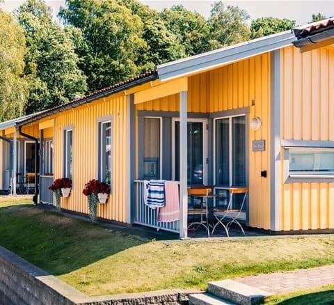 Ett charmigt fritidshus i traditionell stil, omgärdat av lummig grönska, med en rymlig veranda och intilliggande trädgårdsbyggnader i Lisebergsbyn.