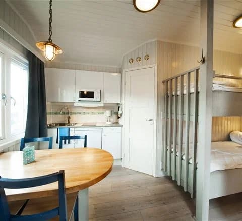 Interiör av ett rum vid Lisebergsbyn, med trägolv och träpaneler i taket. Rummet är möblerat med enkla trämöbler och har mjuk belysning från en taklampa.