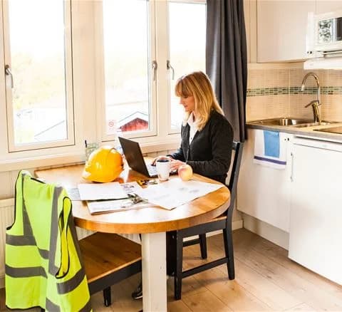 En välkomnande interiör i Lisebergsbyn med moderna möbler. Rummet är inrett med trämöbler, ett bord med stolar och diskreta ljuskällor. Golvet är av trä och skapar en varm atmosfär, medan ett modernt köksområde syns i bakgrunden.