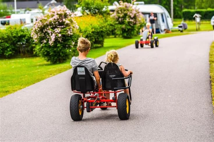 En familj njuter av fritiden på Harge bad & camping, med glada barn som leker och rullar runt på gräsytan. Perfekt semestermål för avkoppling och roliga stunder.