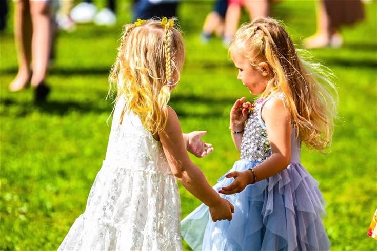 En glad blond flicka i en rosa klänning leker ute i naturen under våren, omgiven av grönt gräs och träd, vilket förmedlar en känsla av frihet och glädje.