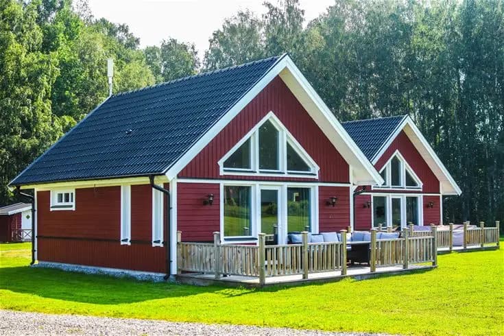 En charmig stuga med rött tak omgiven av grönskande gräsmatta och trädgårdslandskap på Harge Bad & Camping.