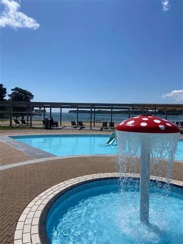 En bild av Harge Bad & Camping visar en semesteranläggning med en blå pool omgiven av utomhusmöbler. Solsängar står i skuggan nära poolen, och den avslappnande atmosfären förstärker känslan av en trevlig semester.