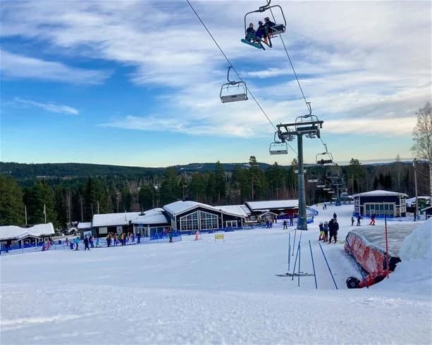 Skidåkare på en snötäckt pist i vinterlandskapet vid Bjursås Berg & Sjö, omgiven av skog och skidutrustning.
