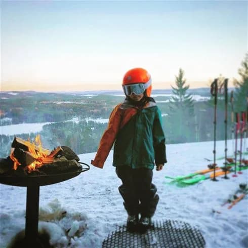 En grupp glada barn leker i snön iklädda vinterkläder och skidutrustning vid Bjursås Berg & Sjö, en populär destination för vinteraktiviteter.