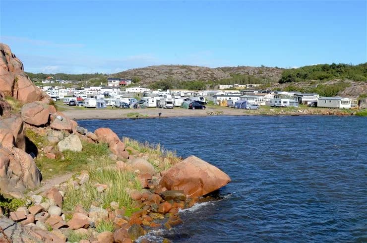 En solig dag vid Siviks camping med utsikt över en vacker kuststräcka med sandstrand och klippor, omgiven av grönt landskap och en blåskimrande havsvik.