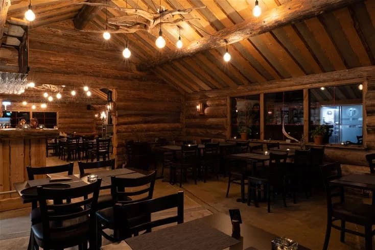 En mysig interiör på Kojbyns camping med träinredning. Bilden visar ett rum med taklampor, bord och stolar, skapar en varm och inbjudande atmosfär.