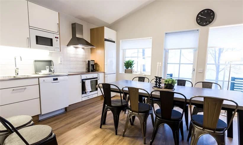 Interiörbild av Mösseberg Camping med trägolv, trätak och en ljus, rymlig känsla. I förgrunden syns stolar och ett bord som del av möblemanget. Ljuset från armaturer ger en hemtrevlig atmosfär.