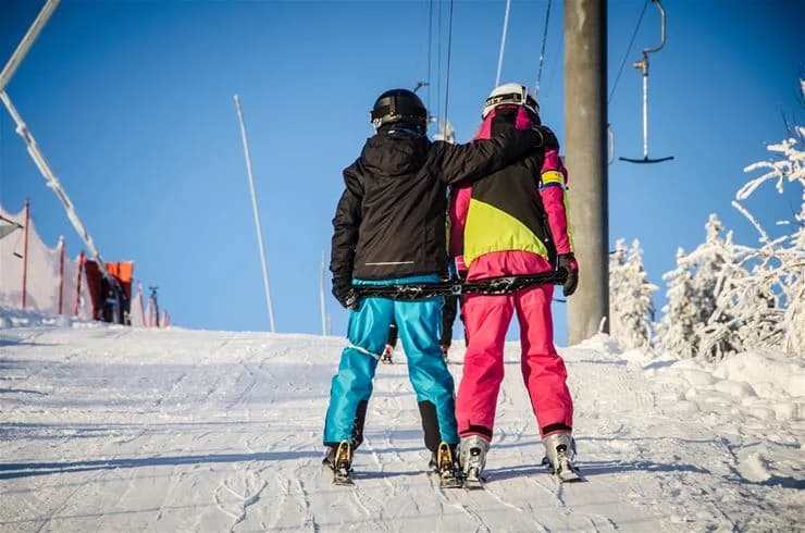 En vinteridyll vid Mösseberg camping med snötäckta omgivningar där en person förbereder sig för vintersport, iklädd skidor och skyddsutrustning, redo för utomhusaktiviteter.
