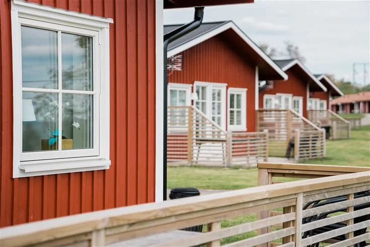 En mysig stuga med träfasad omgiven av en grönskande trädgård på Mösseberg Camping. Det finns en veranda med utemöbler i skuggan, perfekt för avkoppling utomhus.