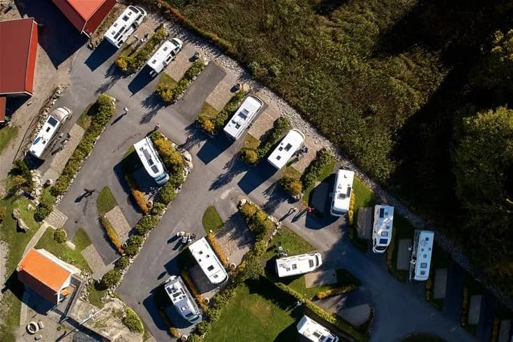 Flygbild över Lagunen Camping & Stugor med välplanerade parkeringsplatser, uppställda husbilar och stugor omgivna av grönska.