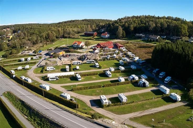 Flygbild över Lagunen Camping & Stugor visar en parkering med husbilar och husvagnar, omgiven av grönska och naturskönt landskap.