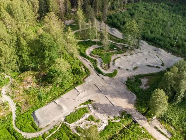 Flygbild över Lagunen Camping & Stugor med en slingrande stig som går genom ett skogsområde med barrträd.