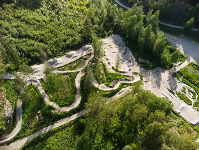 En fågelperspektivvy över en cyklist som kör utför en skogsstig, omgiven av frodig grönska, vid Lagunen Camping & Stugor. Aktivitäten innefattar friluftsliv och äventyrscykling, vilket föreslår möjligheter till mountainbike och BMX-åkning.