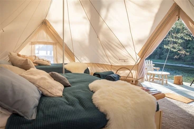 En tältplats vid Lagunen Camping & Stugor med ett uppslaget tält nära vattnet. En båt syns också i bakgrunden, omgiven av grönska och tältutrustning såsom presenningar och sängkläder för rekreation och friluftsliv.