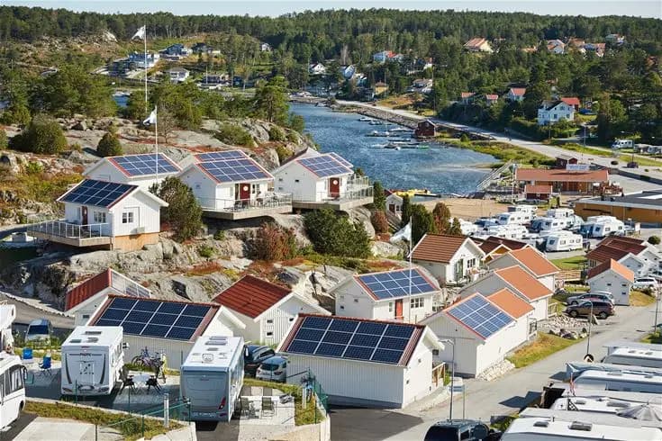 Fågelperspektiv av Lagunen Camping & Stugor, visar stugor och hus med röda tak, omgivna av grönska, belägna nära kusten i en naturskön miljö.