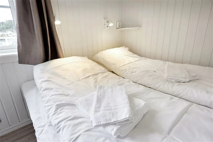 Ett sovrum med träinredning på Lagunen Camping & Stugor. Rummet har ett trägolv och är inrett med en stor säng med vita lakan och trästomme.