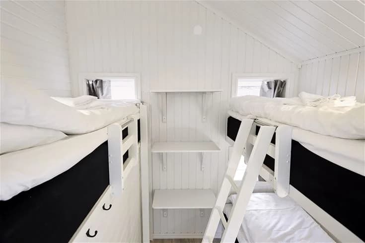 Ett sovrum på Lagunen Camping & Stugor med mysig inredning. Rummet har en dubbelsäng klädd i vita sängkläder, två kuddar och trägolv. Det finns ett ljust tak och en enkel, stilren design som ger en avslappnad atmosfär.