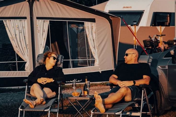 En campingplats med tält, utomhusmöbler och husvagnar under en klar himmel på Gröndals Camping & Stugor, perfekt för rekreation och semester.