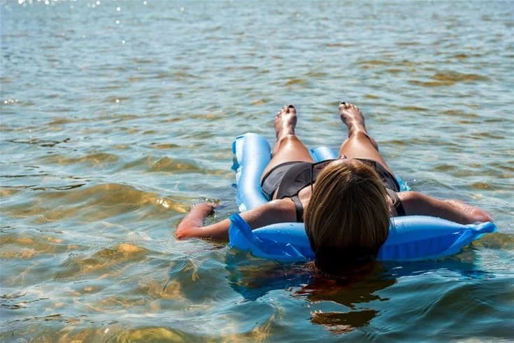 En grupp människor i badkläder njuter av sommaraktiviteter vid Gröndals camping & stugor, där de leker med uppblåsbara leksaker vid en vattenmiljö.