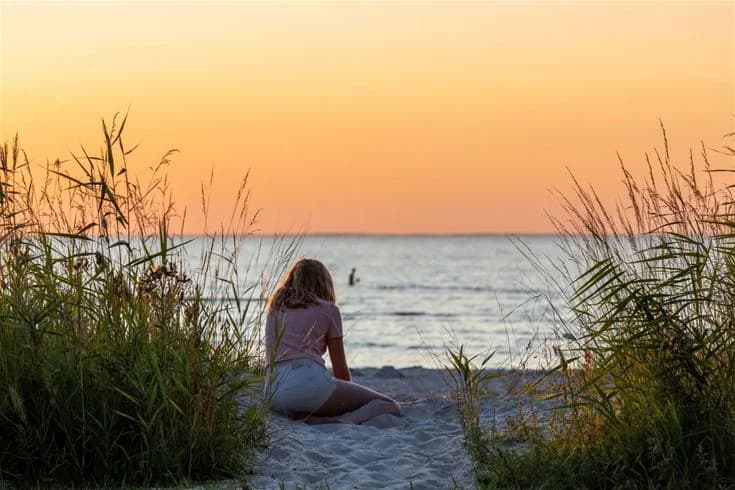 En vacker sommarbild av Gröndals Camping & Stugor visar en solnedgång över havet, med en strand i förgrunden och människor som njuter av den natursköna kustmiljön.