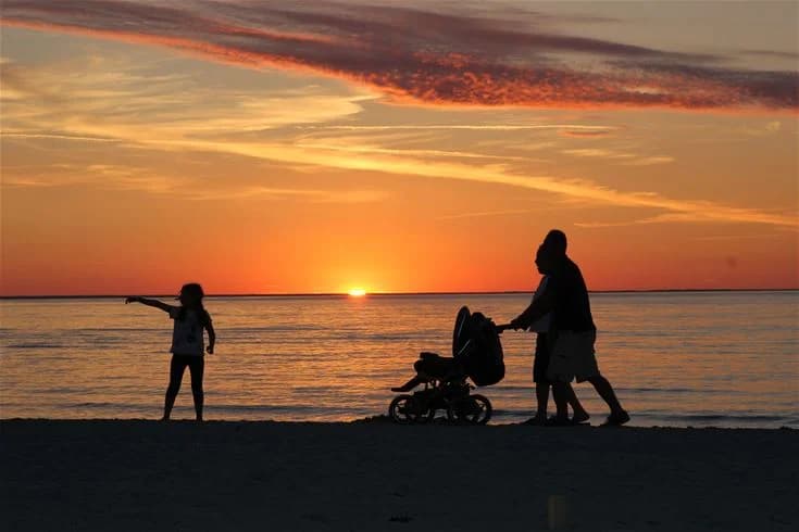 Två personer står vid den orangefärgade horisonten i solnedgången på en strand, med havet i bakgrunden, vid Gröndals Camping & Stugor. 