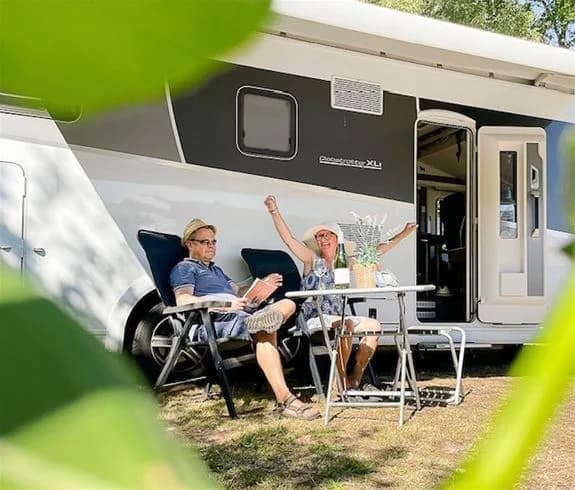 En campingplats i Båstad med husvagnar och campingbilar. Utemöbler och fällstolar står uppställda intill fordonen, vilket skapar en avslappnad och inbjudande atmosfär för rekreation och fritid.